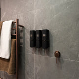 three black ONNYBODY dispensers attached to a tiled bathroom wall.