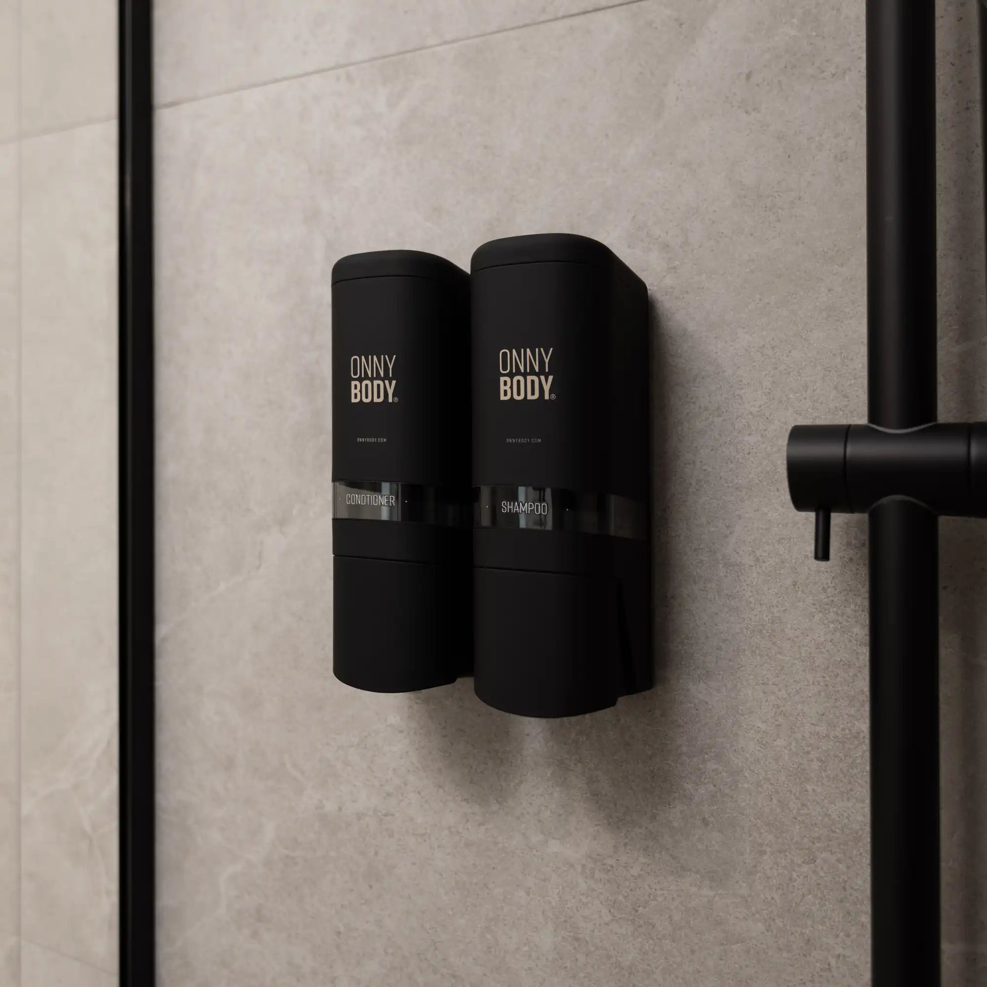 two black ONNYBODY dispensers attached to a tiled bathroom wall.