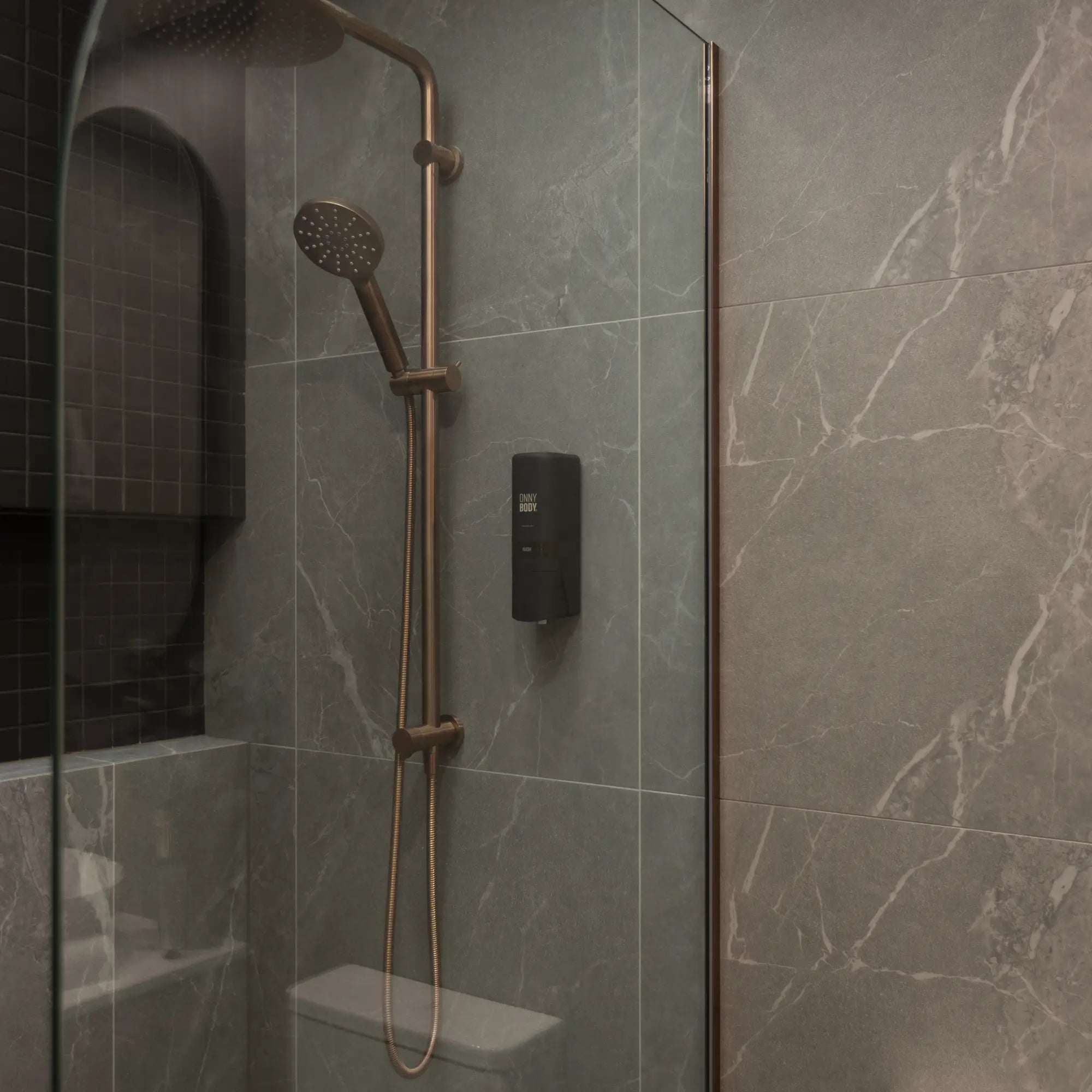 One black ONNYBODY dispenser attached to a tiled bathroom wall next to a shower head.