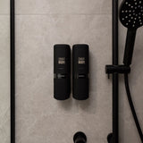 Two black ONNYBODY dispensers attached to a tiled bathroom wall next to a shower head.