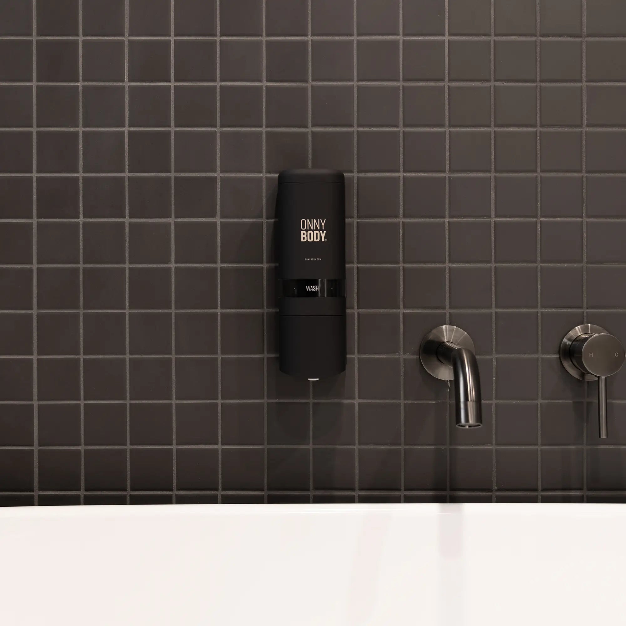 Black ONNYBODY dispenser mounted on a dark tiled wall with silver faucet.